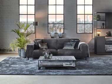 Grijze velvet bank in een industrieel en rustig interieur met een groot vloerkleed.