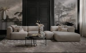 Element sofa Emanuelle with a longchair and an ottoman between the elements. Made from a light beige fabric. Combined with a large rug and natural decoration.