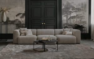 Emanuelle sofa with 3 seats. Made in a beige fabric. Styled with a rug and natural and black decoration.