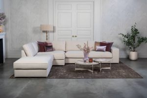 Beige hoekbank met grote hoek, gestyled met woonaccessoires in Burgundy.