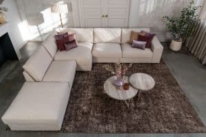 Beige hoekbank met grote hoek, gestyled met woonaccessoires in Burgundy.