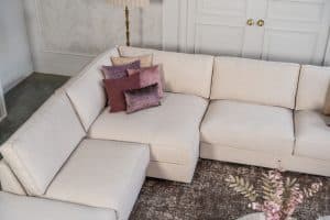 Beige hoekbank met grote hoek, gestyled met woonaccessoires in Burgundy.
