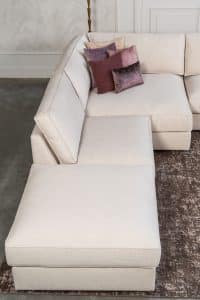 Beige hoekbank met grote hoek, gestyled met woonaccessoires in Burgundy.