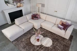 Beige hoekbank met grote hoek, gestyled met woonaccessoires in Burgundy.